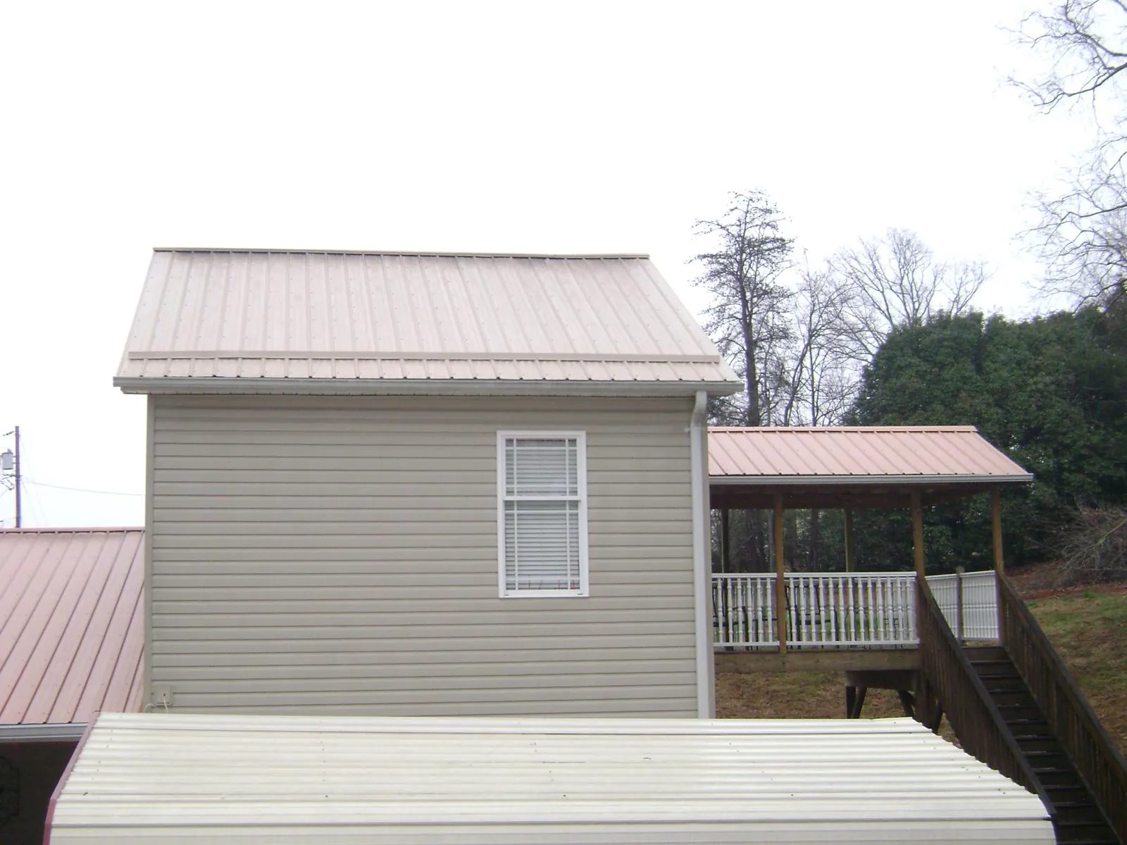 Tan metal roofs on a two story addition and attached porch, from a Roof Replacement job in Hartland
